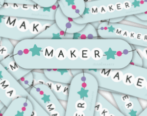 Close-up of pastel-colored earrings with the word 'MAKER'.