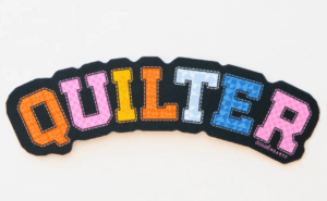 Colorful embroidered word 'QUILTER' on black fabric.